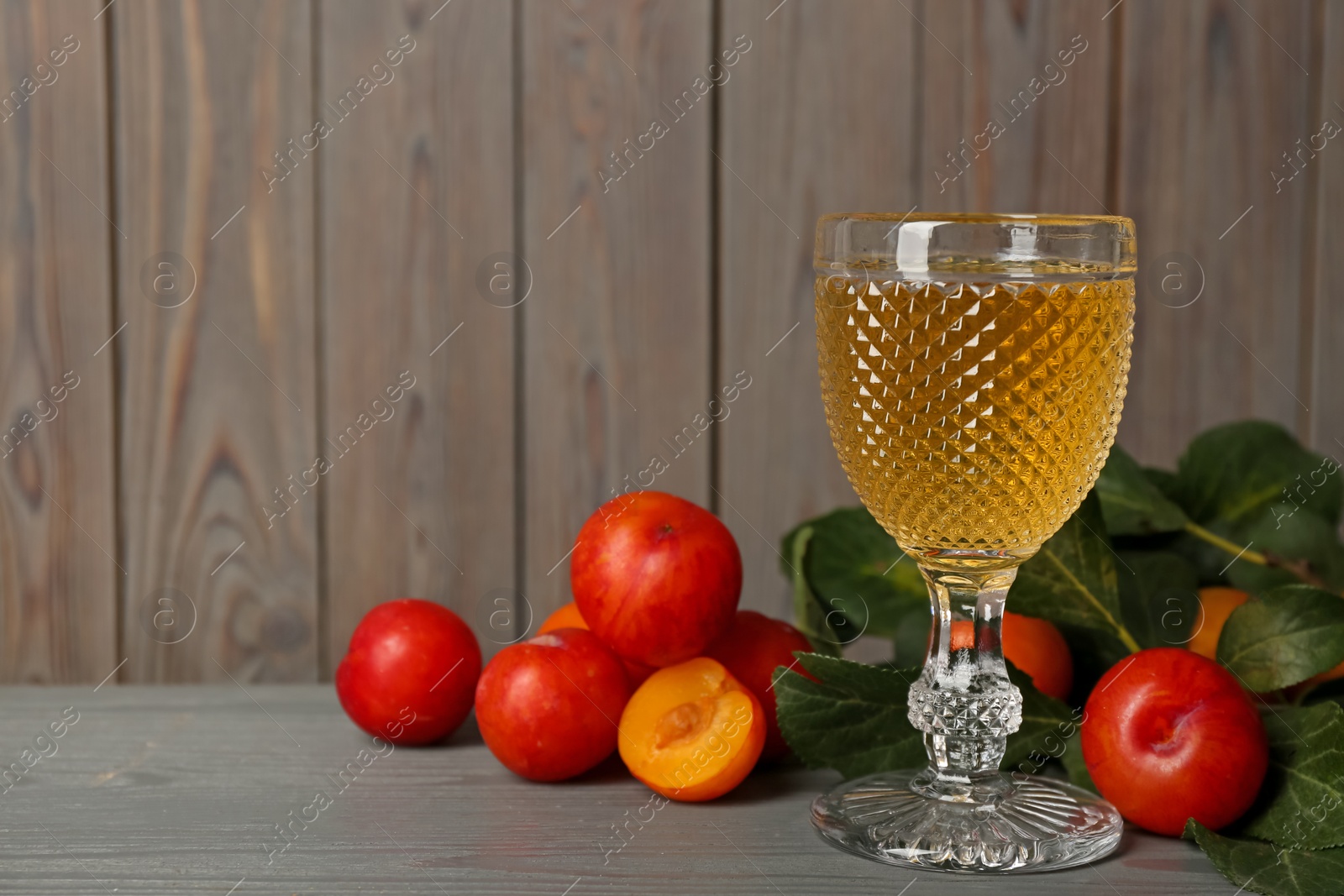 Photo of Delicious plum liquor and ripe fruits on grey wooden table, space for text. Homemade strong alcoholic beverage