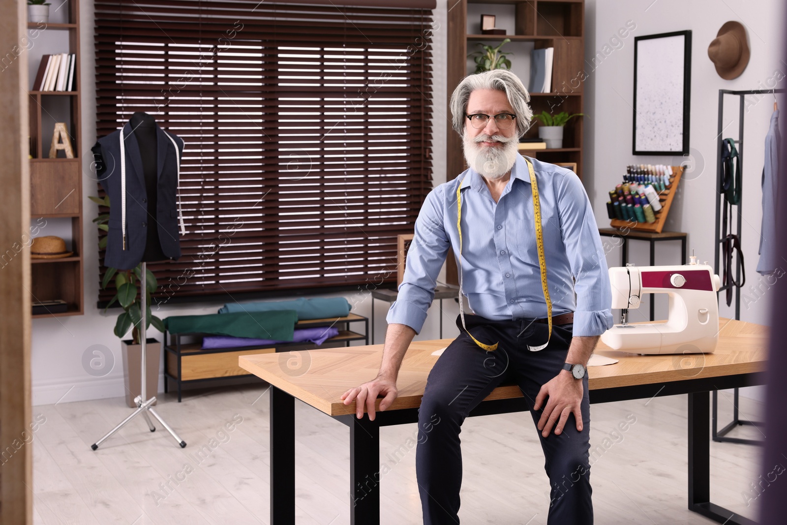 Photo of Professional tailor with measuring tape in workshop, space for text