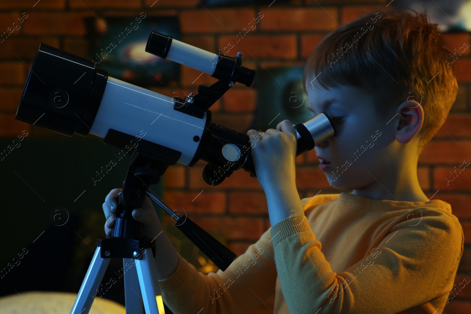 Photo of Little boy looking at stars through telescope in room