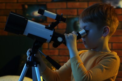 Photo of Little boy looking at stars through telescope in room