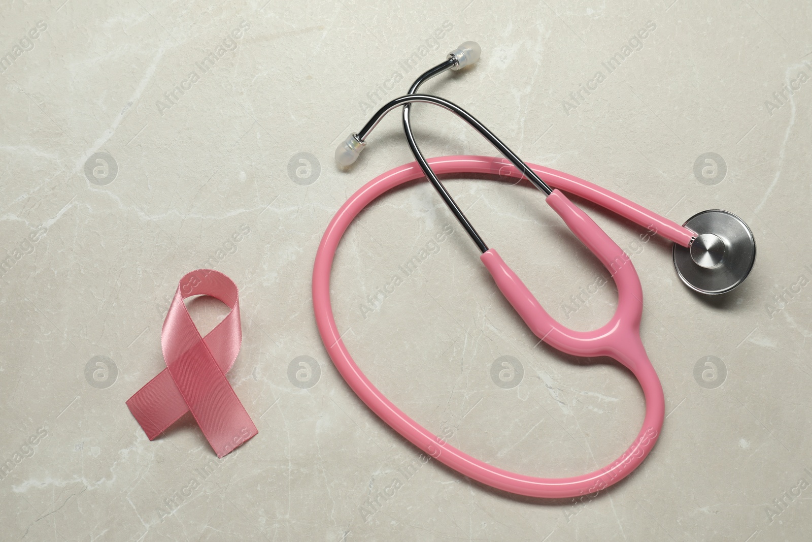 Photo of Pink ribbon and stethoscope on light grey table, flat lay. Breast cancer awareness