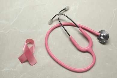 Pink ribbon and stethoscope on light grey table, flat lay. Breast cancer awareness