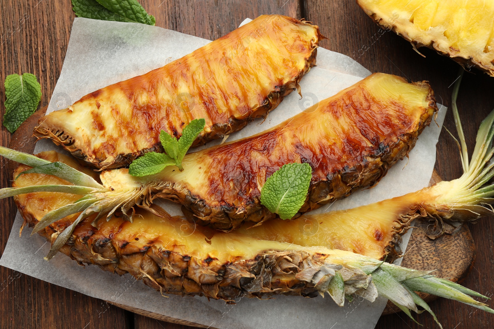 Photo of Tasty grilled pineapple pieces and mint leaves on wooden table, flat lay