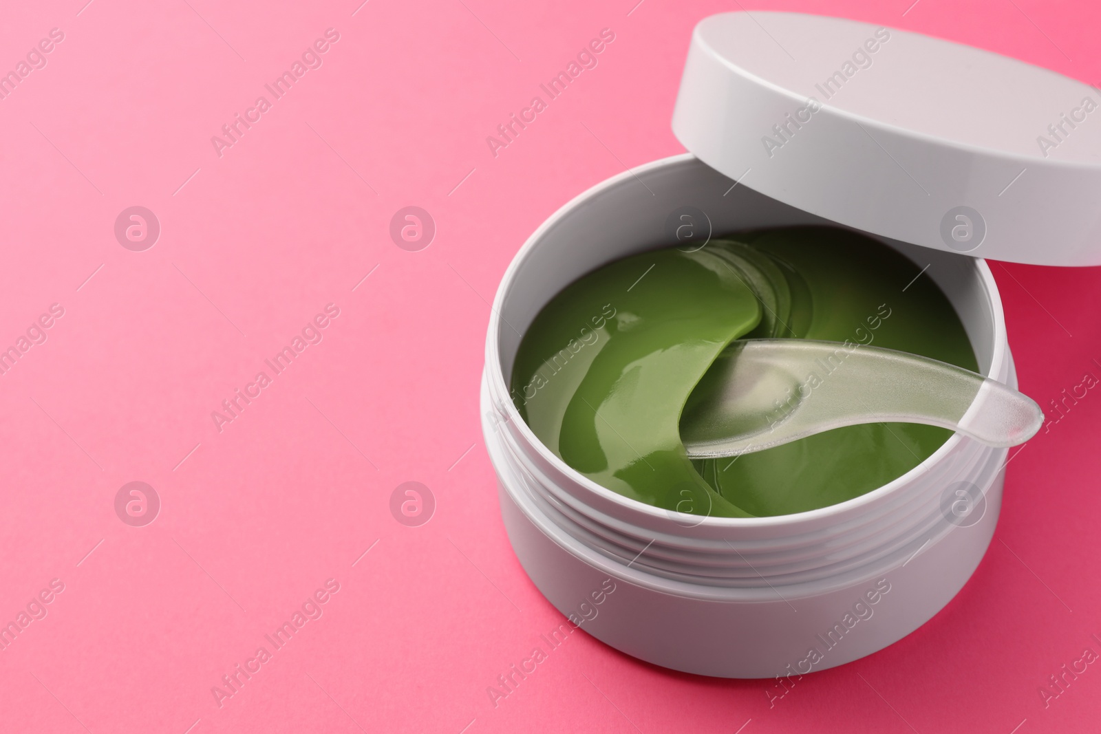 Photo of Jar of under eye patches with spoon on pink background, closeup. Space for text