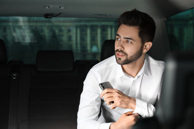 Young man with smartphone on backseat of modern car
