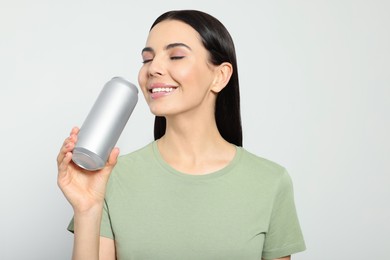 Beautiful happy woman drinking from beverage can on light grey background