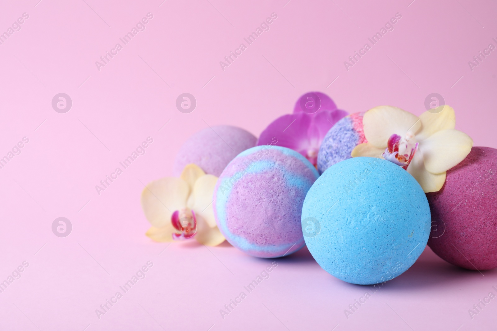 Photo of Colorful bath bombs and beautiful orchid flowers on pink background, space for text