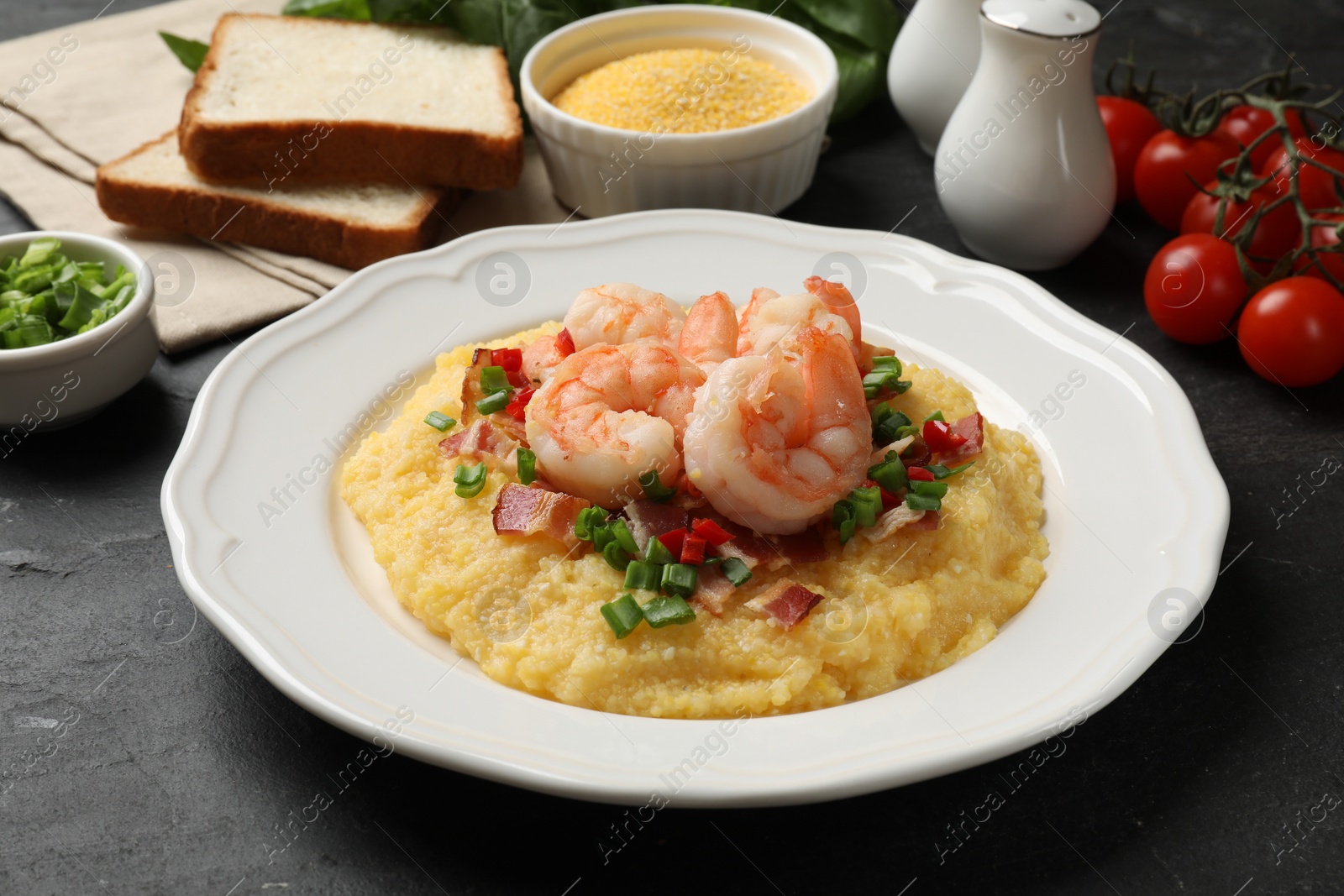 Photo of Plate with fresh tasty shrimps, bacon, grits, green onion and pepper on black table, closeup