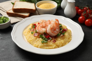 Photo of Plate with fresh tasty shrimps, bacon, grits, green onion and pepper on black table, closeup