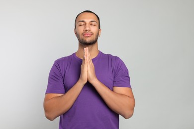 African American man with clasped hands praying to God on light grey background