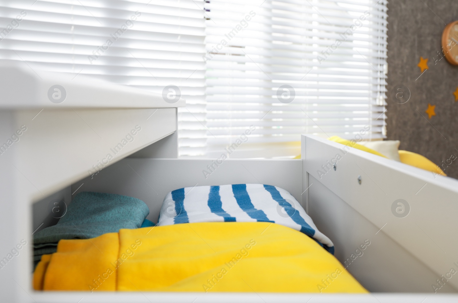 Photo of Modern open chest of drawers with clothes in room, closeup