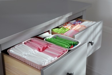 Photo of Open cabinet drawers with menstrual pads, tampons and pantyliners indoors, closeup