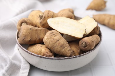 Photo of Whole and cut tubers of turnip rooted chervil in bowl on white tiled table, closeup