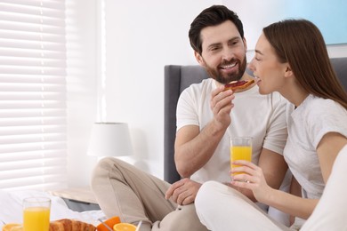 Photo of Tasty breakfast. Happy husband feeding his wife in bedroom. Space for text
