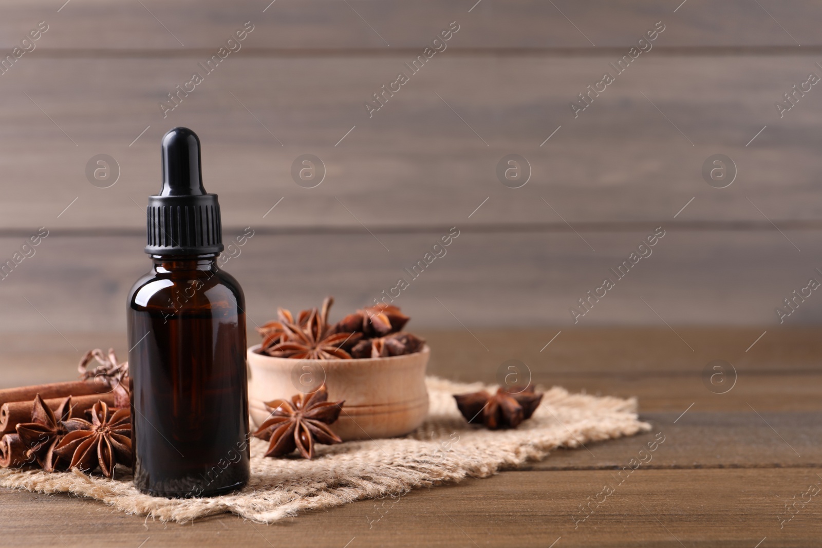 Photo of Anise essential oil and spices on wooden table, space for text