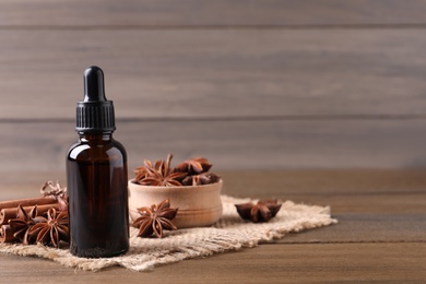 Anise essential oil and spices on wooden table, space for text