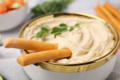 Photo of Delicious hummus with grissini sticks on table, closeup