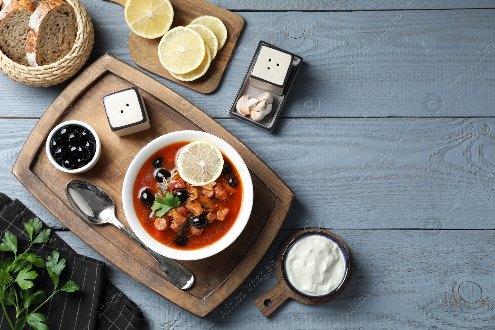 Photo of Meat solyanka soup with sausages, olives and vegetables served on grey wooden table, flat lay. Space for text