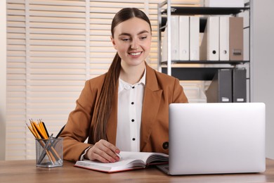 Happy woman taking notes at wooden table in office