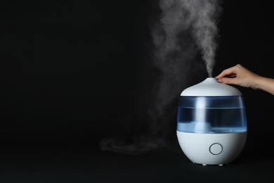 Woman using modern air humidifier on black background, closeup. Space for text