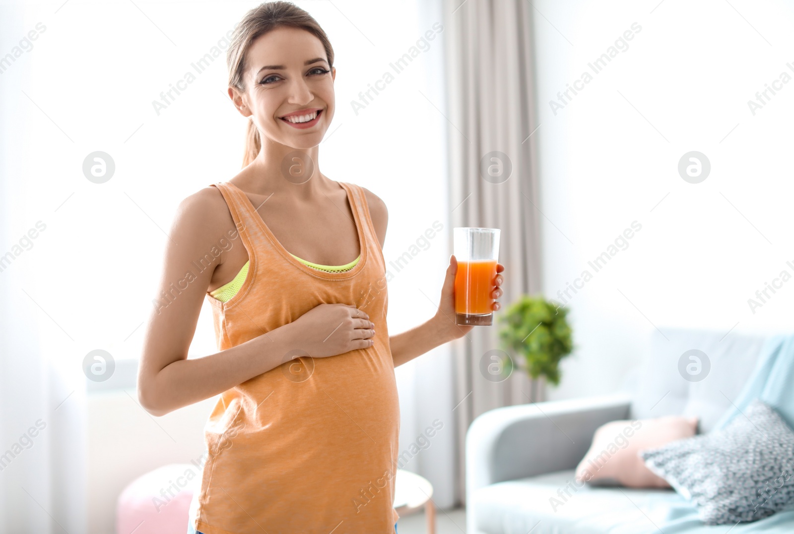 Photo of Young pregnant woman holding glass with juice at home