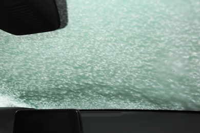 Photo of Automobile windshield covered with foam, view from inside. Car wash service