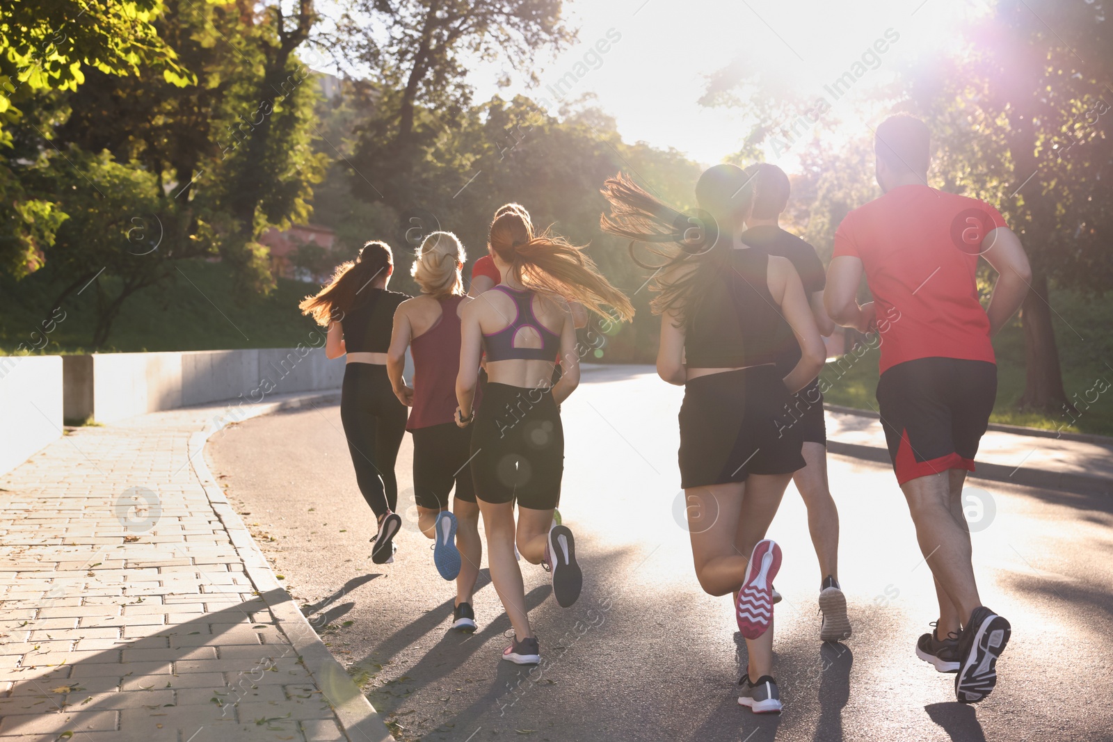 Photo of Group of people running outdoors on sunny day, back view