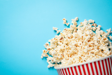 Photo of Overturned paper bucket with delicious popcorn on light blue background, top view. Space for text