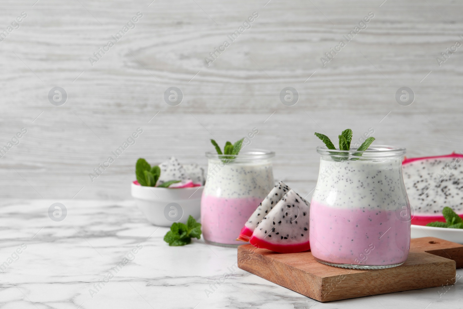Photo of Delicious pitahaya smoothie, fruits and fresh mint on white marble table, space for text