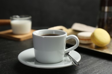 Photo of Hot coffee in cup, saucer and spoon on dark textured table, closeup