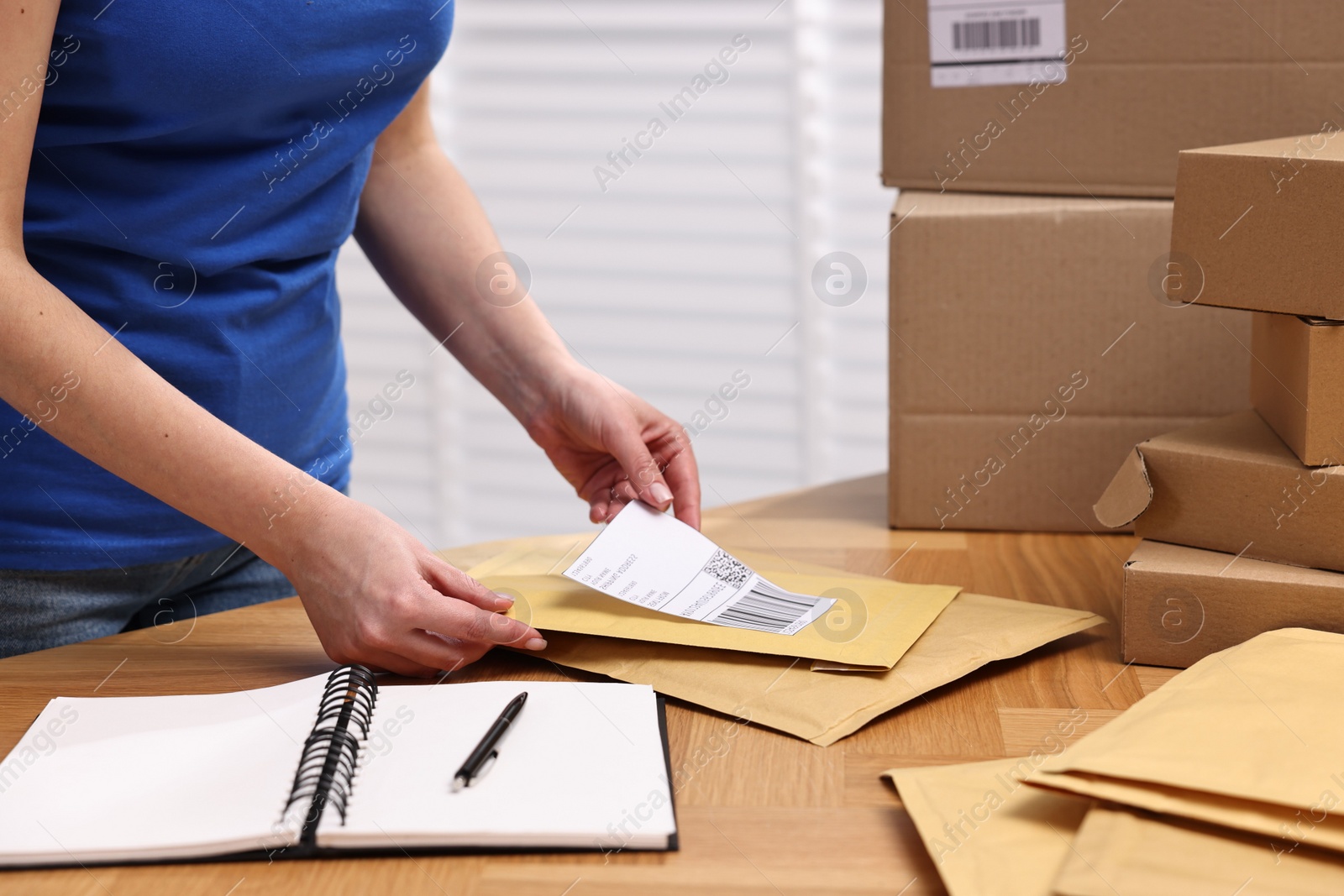 Photo of Parcel packing. Post office worker sticking barcode on bag at wooden table indoors, closeup