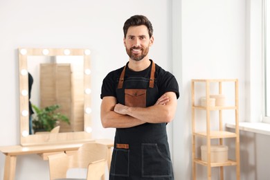 Photo of Smiling handsome hairdresser wearing apron in salon