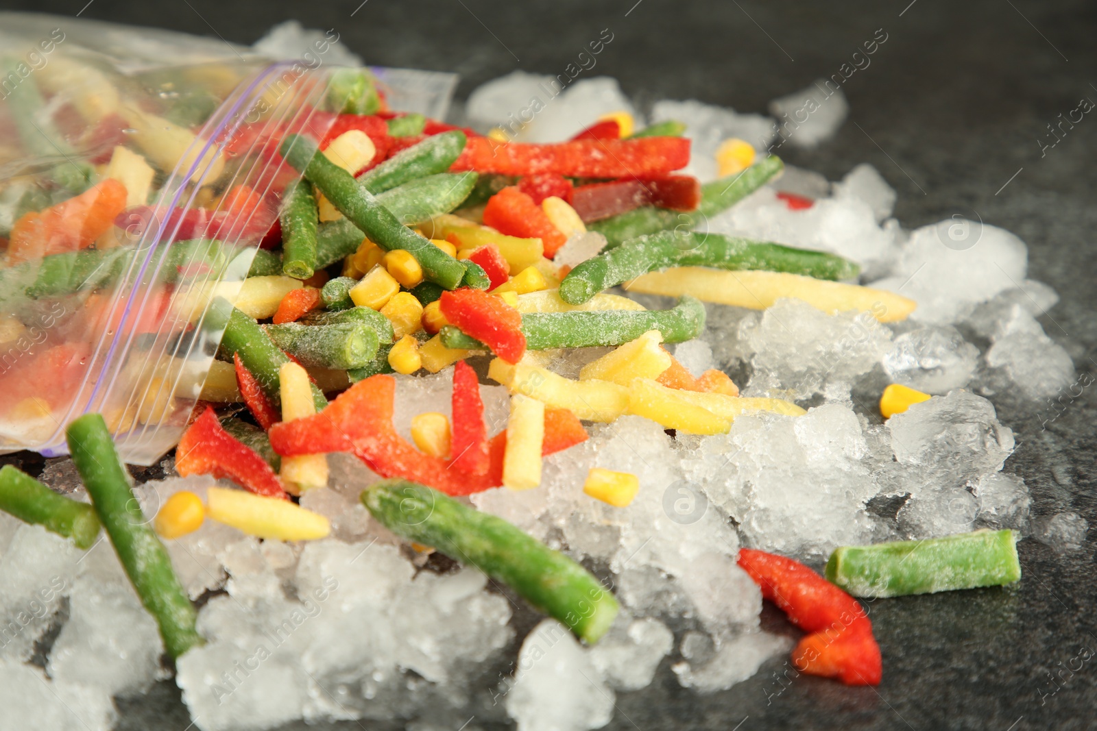 Photo of Zip bag with different frozen vegetables and ice on grey table, closeup