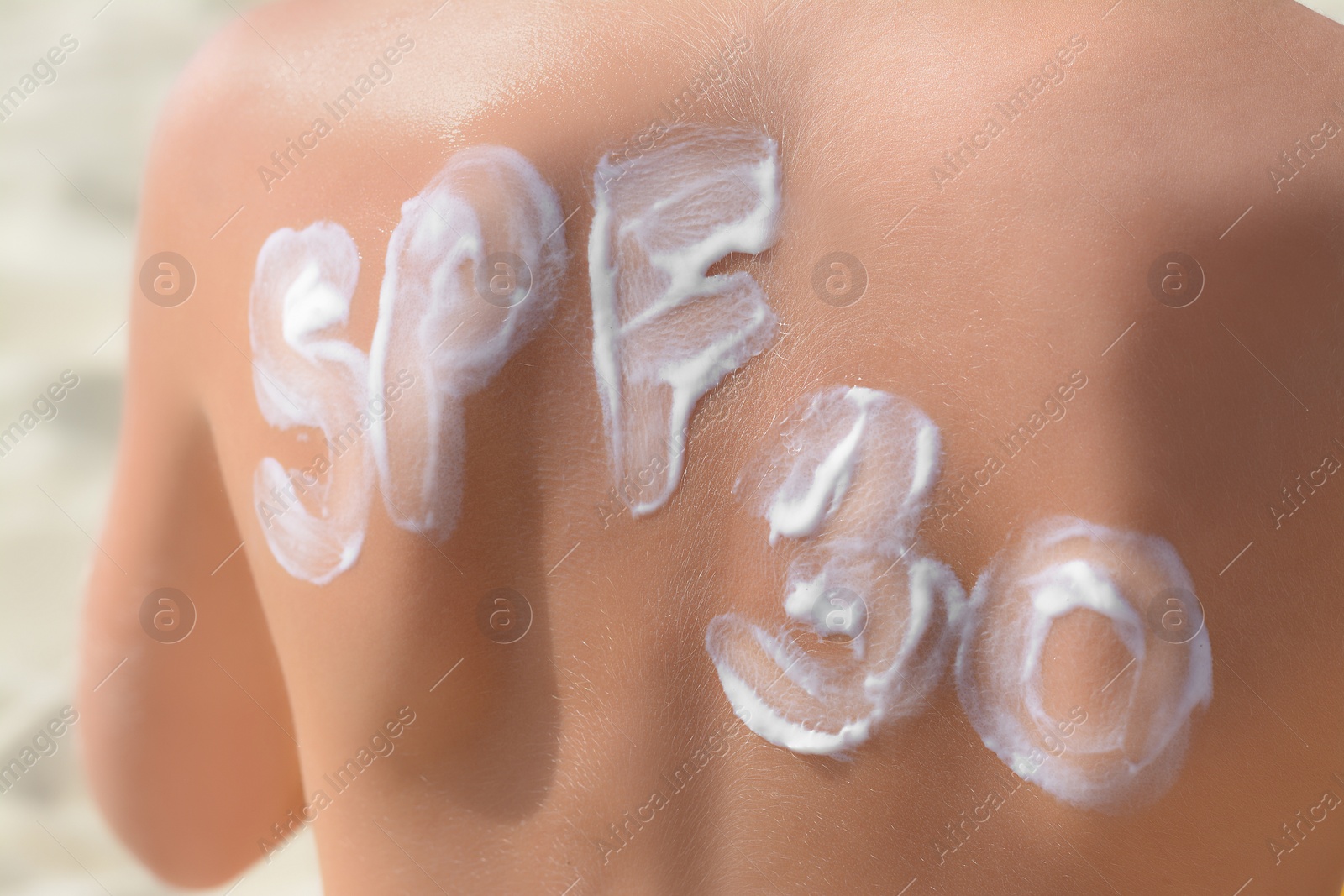 Photo of Child with abbreviation SPF 30 of sunscreen on back at beach, closeup
