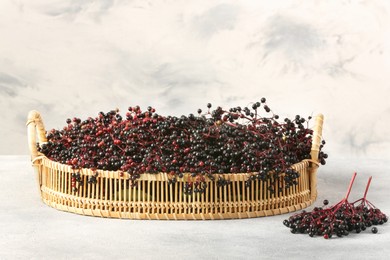 Wicker basket with ripe elderberries on light grey table