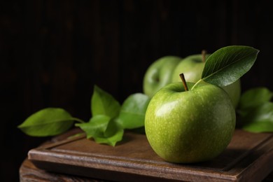 Fresh ripe green apples with leaves on wooden table against black background, closeup