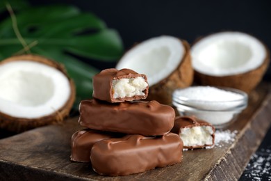 Photo of Delicious milk chocolate candy bars with coconut filling on wooden board, closeup