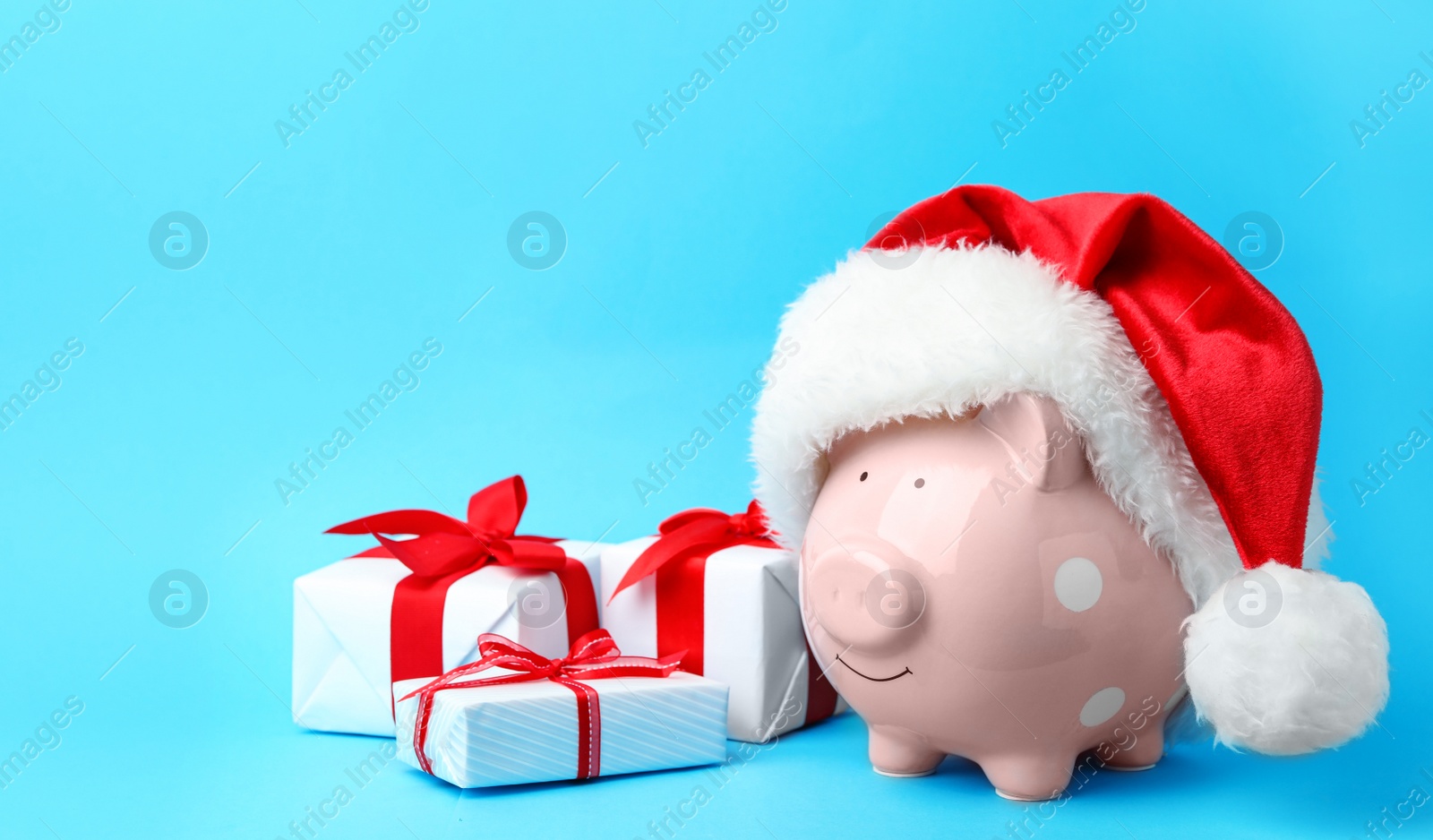 Photo of Piggy bank with Santa hat and gift boxes on light blue background