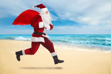 Image of Santa Claus with sack running on sandy beach. Space for text