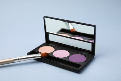 Photo of Beautiful eye shadow palette and brush on light blue violet background
