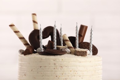 Delicious cake decorated with sweets and candles against blurred background, closeup