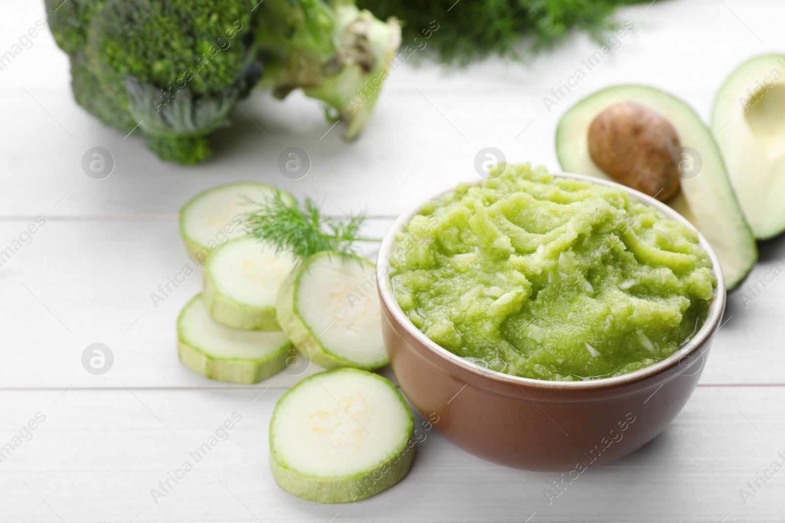 Photo of Bowl with tasty puree, zucchini, avocado and broccoli on white wooden table