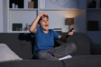 Photo of Emotional boy watching TV and holding remote control on sofa at home