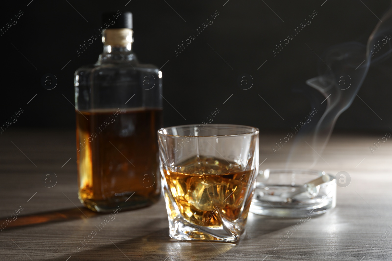 Photo of Alcohol addiction. Whiskey in glass, bottle, cigarettes and ashtray on wooden table