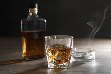 Photo of Alcohol addiction. Whiskey in glass, bottle, cigarettes and ashtray on wooden table