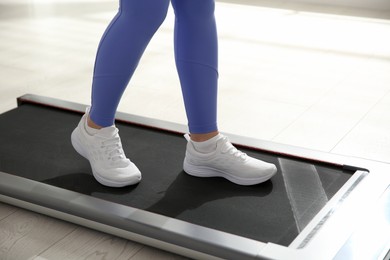 Photo of Sporty woman training on walking treadmill indoors, closeup