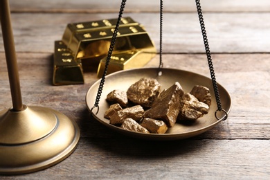 Photo of Scale pan with gold lumps on wooden table, closeup