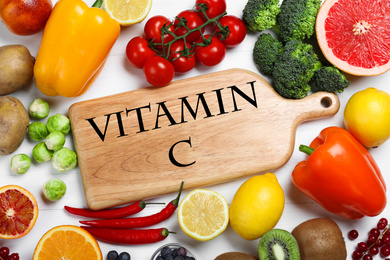 Photo of Board with phrase VITAMIN C and fresh products on white wooden table, flat lay