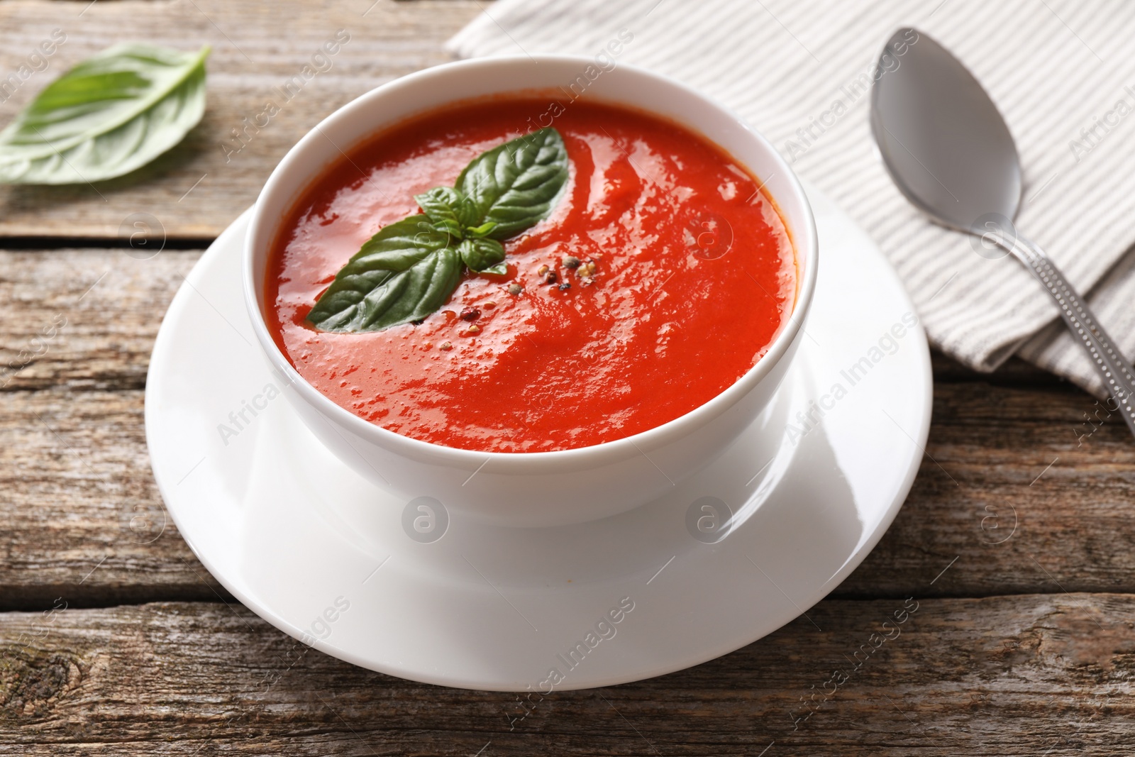 Photo of Delicious tomato soup with basil, spices and spoon on wooden table