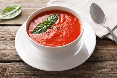 Delicious tomato soup with basil, spices and spoon on wooden table